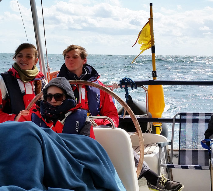 Entspannung im Cockpit im Herbst auf der Ostsee. Vier Gäste mit Rettungswesten beim Mitsegeln.